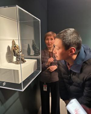 A man leans in to inspect a bronze figurine inside a museum display case.