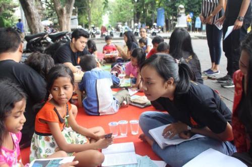 Several young children with a few adults sit outside reading books together.