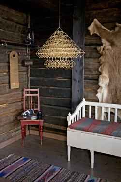 A dimly lit room with an upholstered bench, animal skin wall hanging, striped rag rug, a wash board on the wall, and a geometric straw mobile hanging from the ceiling.