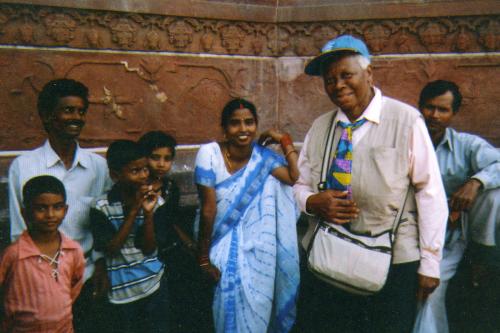 A woman wearing a baseball cap and colorful tie, stands with adults and children, smiling.
