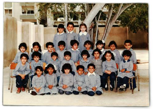 Class photo of several young children in matching gray uniforms. Old color photo.