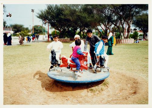 Kids play on a carousel feature in an outdoor park. Old color photo.