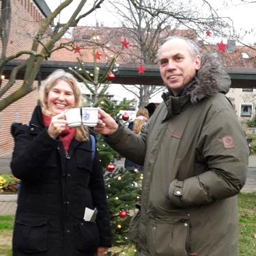 A couple smiles and clinks mugs of mulled wine.