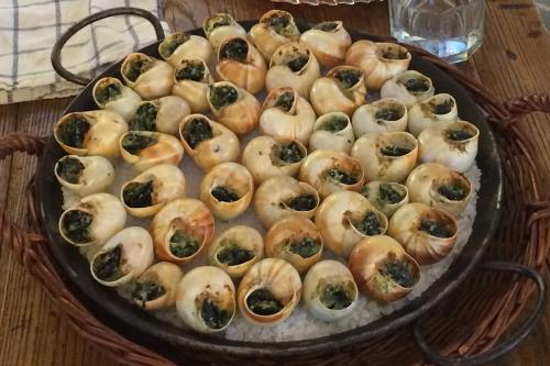 A circular, dark metal paella pan holding chunky white rock salt and dozens of pale brown escargots shells, each stuffed with a dark green mixture.