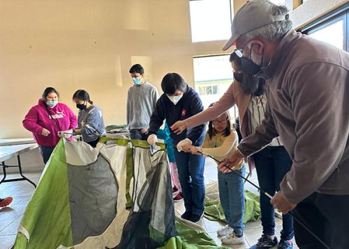 Kids and adults set up a camping tent indoors.
