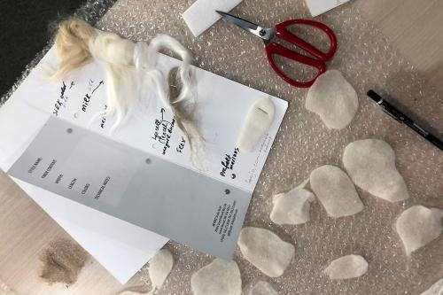 Small pieces of white felt and a card distinguishing four kinds of raw textile fibers, arranged on a piece of bubble wrap on a table.