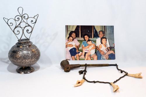 Display of a silver spherical container carved with floral design, a family photo, and a metal pipe on a chain also containing stained white teeth.