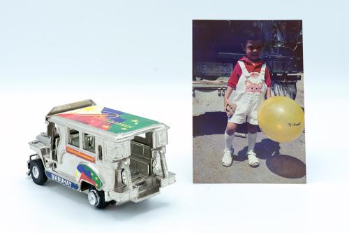 A silver toy truck with the words Philippines on the top and Mabuhay on the side, next to a photo of a young boy with a yellow balloon.
