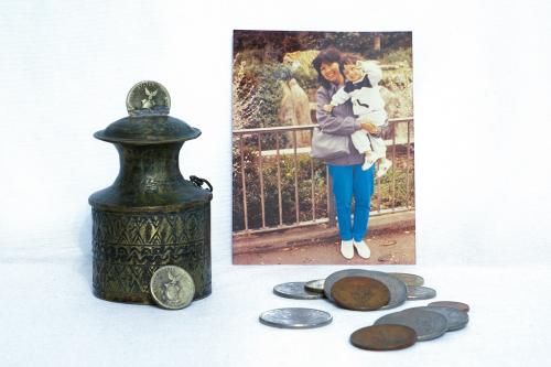 Display of tarnished metal container, scattered silver and bronze coins, and an old photo of a mom holding up a toddler.