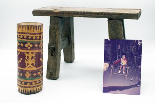 A small wooden bench, displayed with a decorated bamboo container with geometric pattern in dark red, black, and green, and a photo of a young boy sitting on a similar bench, with green bamboo stalks in the background.