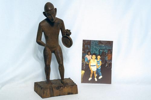 On the left, carved wooden figurine of a person holding a frying pan-shaped object. On the right, photo of kids in a living room.