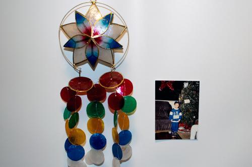 On the left, an ornament with a star/flower shape in white, blue, and pink on top, and red, green, yellow, blue, and white circular shells cascading down. On the right, photo of a boy standing in front of a Christmas tree. A large start ornament hangs in 