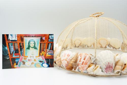 On the left, photo of plates of food set on a table in front of an image of Jesus Christ. On the right, a domed cover for setting over food, lined along the bottom with white and pink seashells.