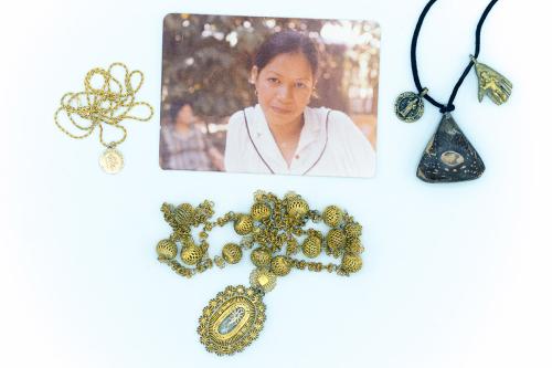 A photo of a woman in white blouse and gold earrings. Around it, three pieces of  metal jewelry: a gold necklace with coin, gold necklace with spherical shapes, and necklace with dark brown triangular shape, golden figure of a saint, and shape of a hand i