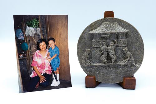 On the left, a photo of a young boy and woman kneeling in a wood-paneled room. On the left, a dark gray circular slab, carbed with a scene of people dancing in front of a hut.