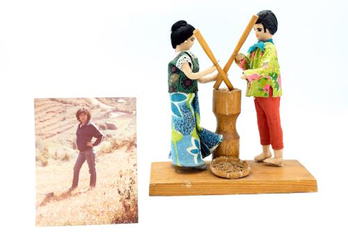 On the left, a photo of a woman standing in on a grassy hillside. On the right, figurine of woman and man in patterened cloths using wooden beaters to pound rice in a wooden container.