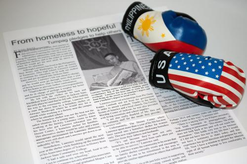 Printout of a newspaper article with the headline: From homeless to hopeful: Tumpag pledges to help others. On top of the paper, a pair of toy boxing gloves, one with the Philippines flag design and the other with American flag.