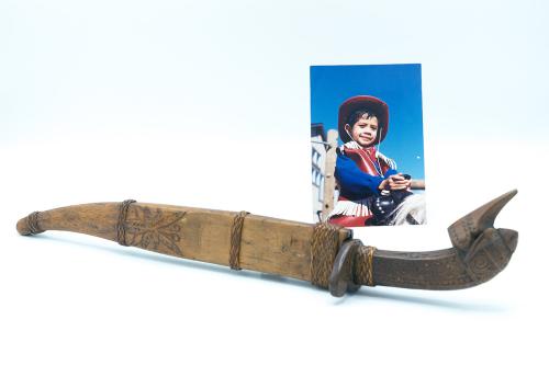 An old dagger in wooden sheath carved with a leaf design. Behind it, photo of a boy in cowboy costume.