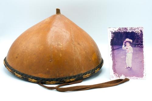 On the left, hat made from half of a dried brown gourd, with a brown cord strap. On the right, old photo  of a kid wearing a brimmed hat.