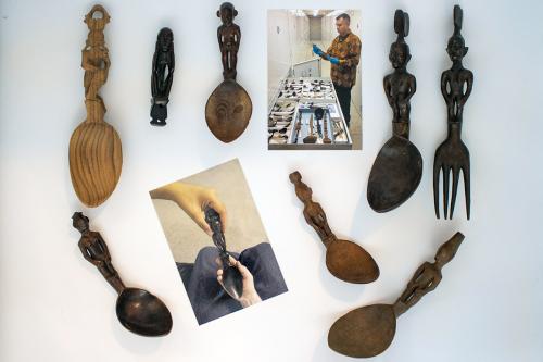 Two photos: in one, a man wearing blue latex gloves handles an object in a museum collection. In front of him, boxes full of carved wooden spoons arranged on a table. In the other, closeup on bare hands holding a dark wooden spoon. Around the photos, eigh