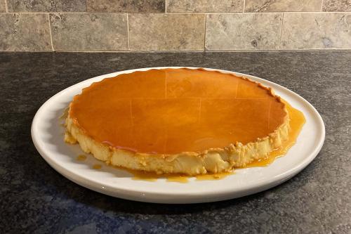 A circular pudding on a white plate with caramel topping, drizzling down the sides.