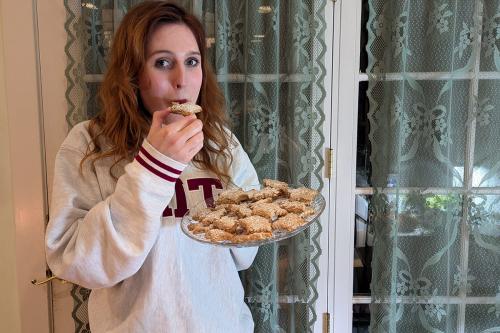 Still holding the plate of cookies, the young woman takes a bite of one.