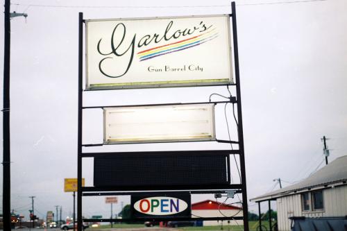 Sign for Garlow’s, written in script and underlined by a rainbow, on an overcast day along a rural street.
