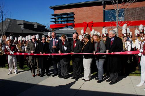 Ribbon-cutting ceremony in front of a brick building, which is also adorned with an oversize red ribbon and bow.