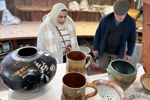 A woman and a man look at shelves of ceramics in a studio room.