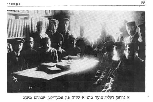Old black-and-white portrait of a group of people sitting around a table. Printed caption is in Hebrew.