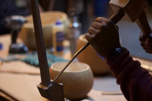 Close-up on a pair of hands chiseling at a piece of wood.