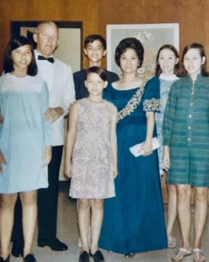A Filipina mother and white father pose with five of their children, all in formal wear. Old color photograph. 