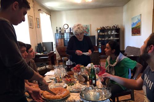 Older woman and teens talk around a table full of food and drink.