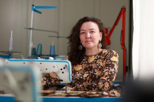 A woman poses, sitting at a sewing machine.