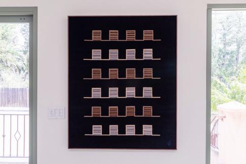 Woven wall hanging between two bright windows. The piece is a black rectangle with alternated rows of brown and gray squares in a sort of grid.