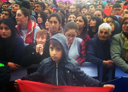 At the front of a crowd of people, a young boy holds up a flag.