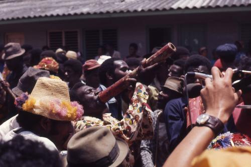 A group of mostly African women, and a white man and woman, dance together outdoors.