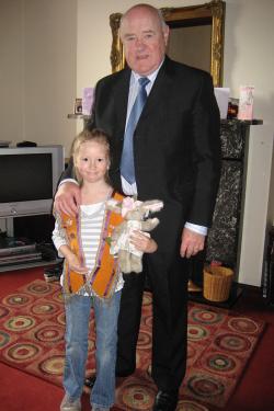 A young girl in orange sash, holding a stuffed rabbit, poses with a man in black suit.