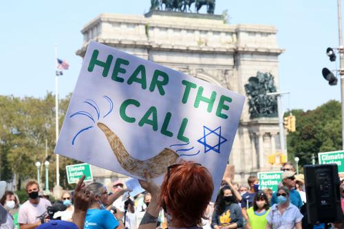 Rally at Washington Square Park, with the marble arch in the background. In the foreground, someone holds up a handmade protest sign that reads HEAR THE CALL with a drawing of a shofar (horn) and Star of David.