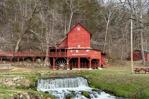 Old red mill building among bare trees, with a stream in the foreground.