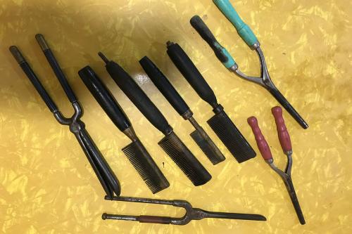 Four black metal combs with thick handles and four sets of hair straightening tools, the shape of pliers with long handles. 
