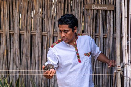 A man rubs a dark ball of wax along a string pulled tight horizontally in front of him.