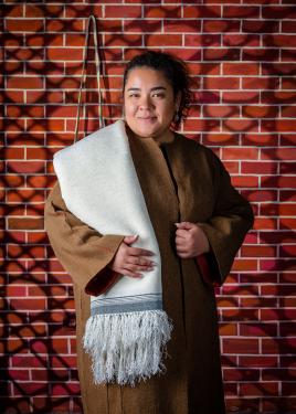 A woman poses a brown robe and white shawl over one shoulder.