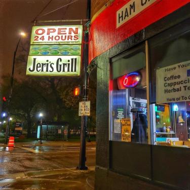 Exterior of the diner on a rainy night. The neon signs reads OPEN 24 HOURS, Jeri’s Grill.
