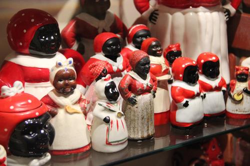 Several ceramic mammy dolls, all in red blouses and  headscarves and white aprons, lined up on a museum display shelf.