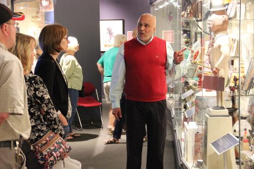 Museum founder David Pilgrim points at objects in a display case, talking with visitors.