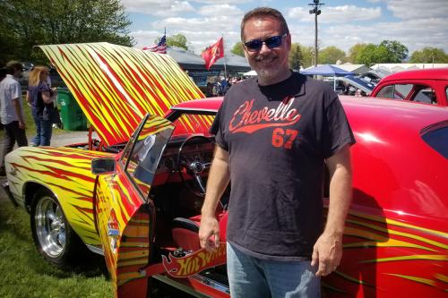 A man stands next to a classic car painted red with yellow flames.