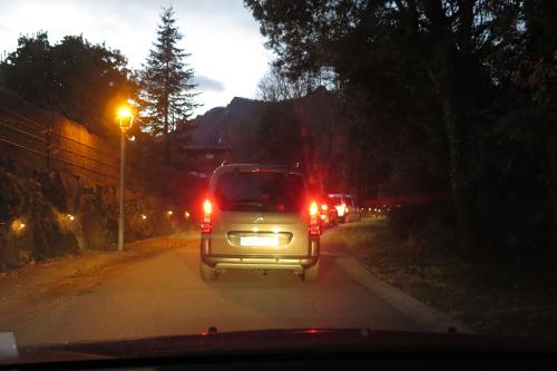 View of a line of cars at dusk on a one-lane road, from inside another car.