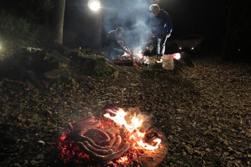 In the foreground, coils of sausage cooking on a firepit; in the background, two men tend another fire.