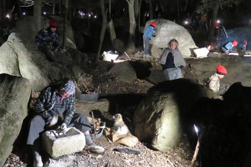 At night, people sit around an outcropping of rock, some chiseling away.